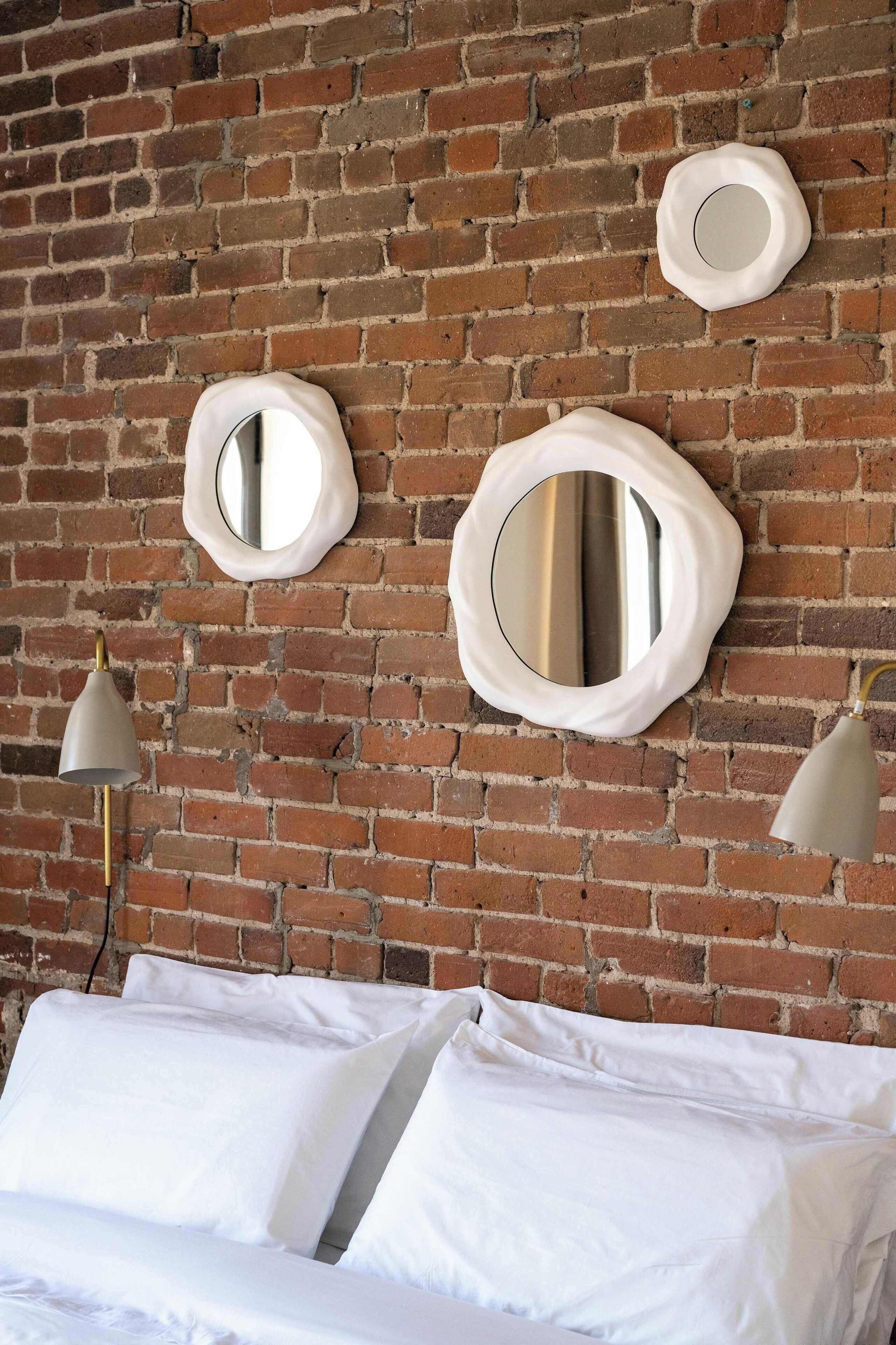 A room with a brick wall, two round mirrors, and a bed with white bedding.