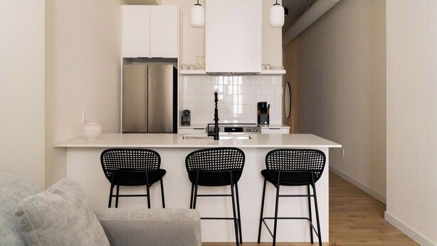 A modern kitchen with a central island, three black bar stools, white cabinets, and pendant lighting. - Maison Place Jacques-Cartier • Luxury Loft • Old Montreal • Self Check-In Access • Full Kitchen • Wi-Fi • AC (Montréal)