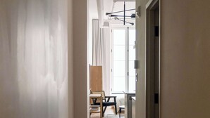 A hallway with a wooden floor, white walls, and a ceiling with exposed ductwork. There is a door on the right and a window with curtains in the background. - Maison Place Jacques-Cartier • Luxury Loft • Old Montreal • Self Check-In Access • Full Kitchen • Wi-Fi • AC (Montréal)