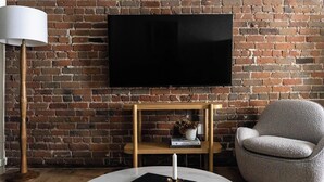 A modern living room with a brick wall, a flat-screen TV, a round coffee table, a grey armchair, and a floor lamp. - Maison Place Jacques-Cartier • Luxury Loft • Old Montreal • Pet Friendly • Full Kitchen • Wi-Fi • AC (Montréal)