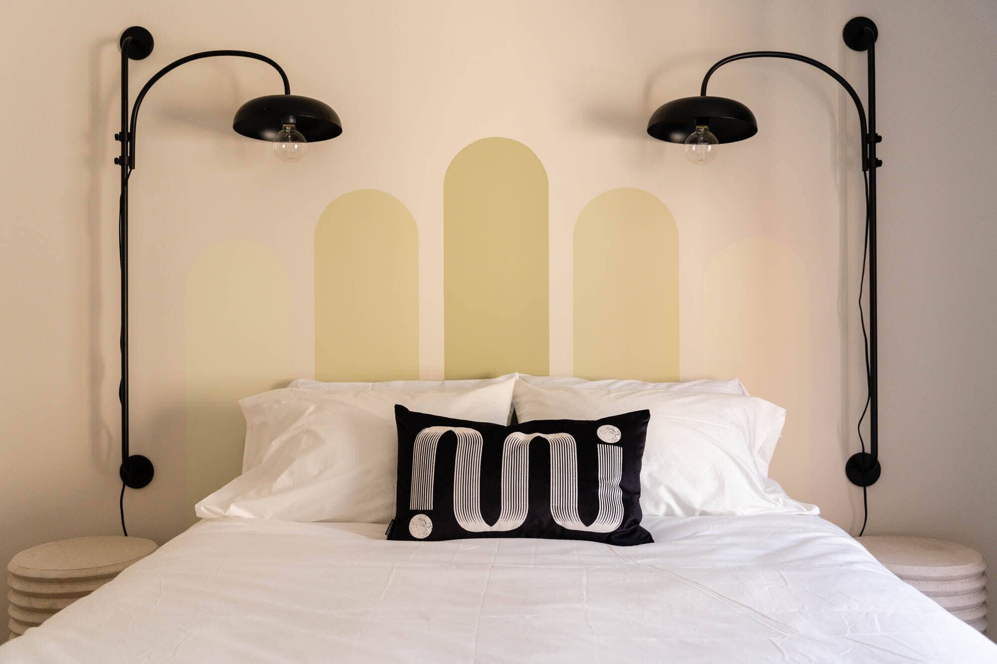 A bed with white bedding, a black pillow with a white design, and two black wall-mounted lamps.