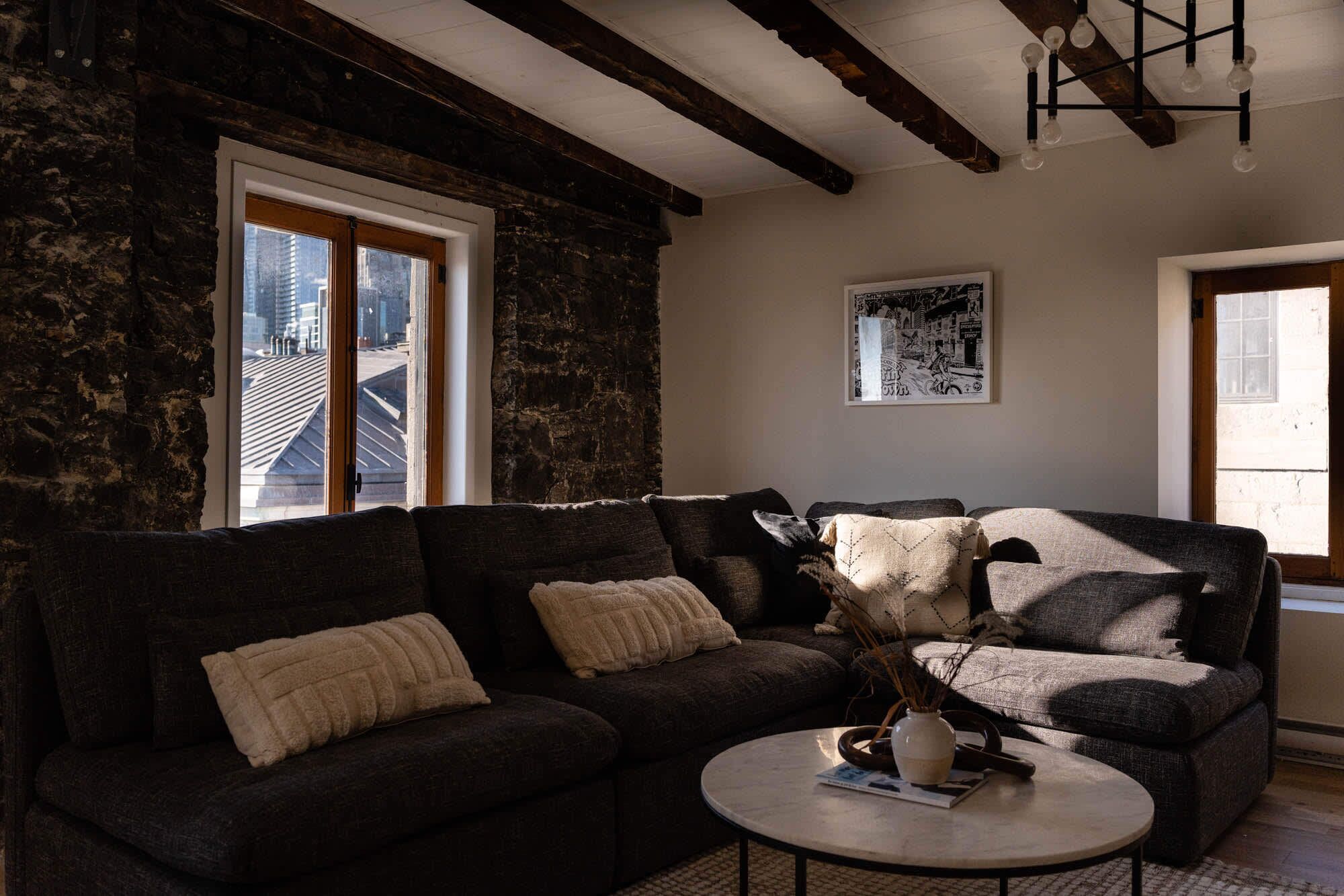 A cozy living room with a dark-colored sofa, a round coffee table, and a large window with a view of a building.