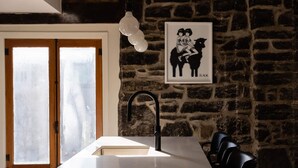 Una cocina con encimera blanca, grifo negro, ventana con vidrio esmerilado y pared de piedra.