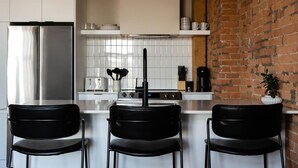 A kitchen with a stainless steel refrigerator, a white tiled backsplash, a black faucet, and a brick wall. - Maison Place Royale • Luxury Waterfront One-Bedroom Apartment • Old Montreal • Water View St. Lawrence River • Full Kitchen • Stone Walls • Wi-Fi • AC (Montréal)