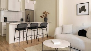 A modern kitchen with a central island, black bar stools, a white sofa, and a framed abstract artwork on the wall.