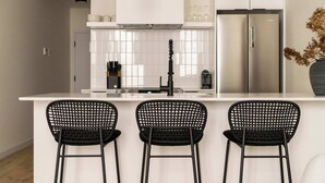 A modern kitchen with white cabinets, a stainless steel refrigerator, and three black mesh chairs.
