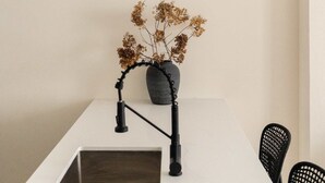 A modern kitchen with a white countertop, a black faucet, and a vase with dried flowers.