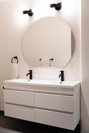 A modern bathroom with a white vanity, black faucets, and a round mirror. - Maison Place Jacques-Cartier • Luxury Loft • Old Montreal • Walk to Restaurants & Shops • Full Kitchen • Wi-Fi • AC (Montréal)