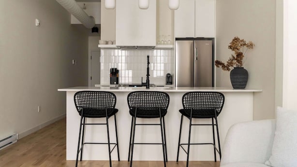 A modern kitchen with white cabinets, a stainless steel refrigerator, and three black bar stools.