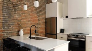 A modern kitchen with a brick wall, white cabinetry, a stainless steel refrigerator, and a built-in oven. - Maison Place Jacques-Cartier  • Luxury Loft • Old Montreal • Central • Full Kitchen • Skylight • Wi-Fi • AC (Montréal)