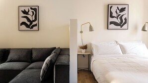 A modern bedroom with a grey sectional sofa, a white bed, and two abstract art pieces on the walls. - Maison Place Jacques-Cartier • Luxury Loft • Old Montreal • Central • Full Kitchen • Skylight • Wi-Fi • AC (Montréal)
