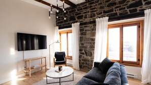 Una sala de estar moderna con pared de piedra, un televisor grande, un sofá, una mesa de centro y una silla.