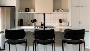 A modern kitchen with white cabinets, a stainless steel refrigerator, a gas stove, and three black chairs. - Maison Place Royale • Luxury Two-Bedrooms Apartment • Old Montreal • Full Kitchen • Stone Walls • Wi-Fi • AC (Montréal)