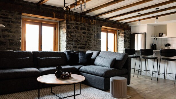 A living room with a sectional sofa, a round coffee table, and a kitchen area with bar stools. - Maison Place Royale • Luxury Two-Bedrooms Apartment • Old Montreal • Full Kitchen • Stone Walls • Wi-Fi • AC (Montréal)