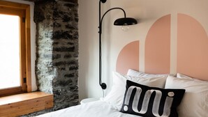 A bedroom with a stone wall, a bed with white bedding, a black lamp, and a large abstract wall design. - Maison Place Royale • Luxury Two-Bedrooms Apartment • Old Montreal • Full Kitchen • Stone Walls • Wi-Fi • AC (Montréal)