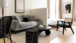 A modern living room with a grey sofa, a black coffee table, and a black chair. There is a framed artwork on the wall and a window with curtains. - Maison Place Jacques-Cartier • Luxury Loft • Old Montreal • Central • Full Kitchen • Wi-Fi • AC (Montréal)