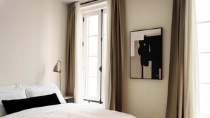A hotel room with a bed, a nightstand, a lamp, a window with curtains, and a framed picture on the wall. - Maison Place Jacques-Cartier • Luxury Loft • Old Montreal • Central • Full Kitchen • Wi-Fi • AC (Montréal)