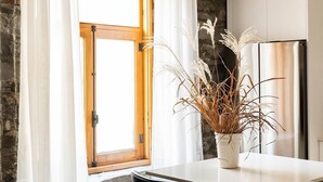 A kitchen with a wooden ceiling, a window with white curtains, a stainless steel refrigerator, and two black chairs. - Maison Place Royale • Luxury Two-Bedrooms Apartment • Old Montreal • Full Kitchen • Stone Walls • Wi-Fi • AC (Montréal)