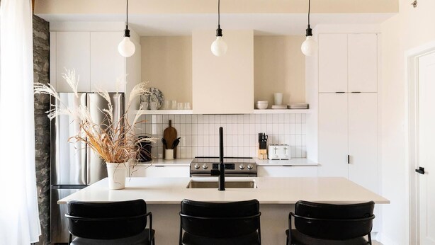 A modern kitchen with white cabinets, a central island with seating, hanging pendant lights, and a stone wall. - Maison Place Royale • Luxury Two-Bedrooms Apartment • Old Montreal • Full Kitchen • Stone Walls • Wi-Fi • AC (Montréal)