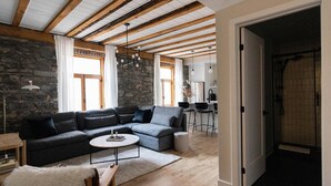 A modern living room with a sectional sofa, a small round coffee table, a stone wall, wooden beams, and a kitchen in the background. - Maison Place Royale • Luxury Two-Bedrooms Apartment • Old Montreal • Full Kitchen • Stone Walls • Wi-Fi • AC (Montréal)