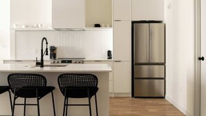 Una cucina moderna con mobili bianchi, un frigorifero in acciaio inossidabile e due sgabelli da bar neri.
