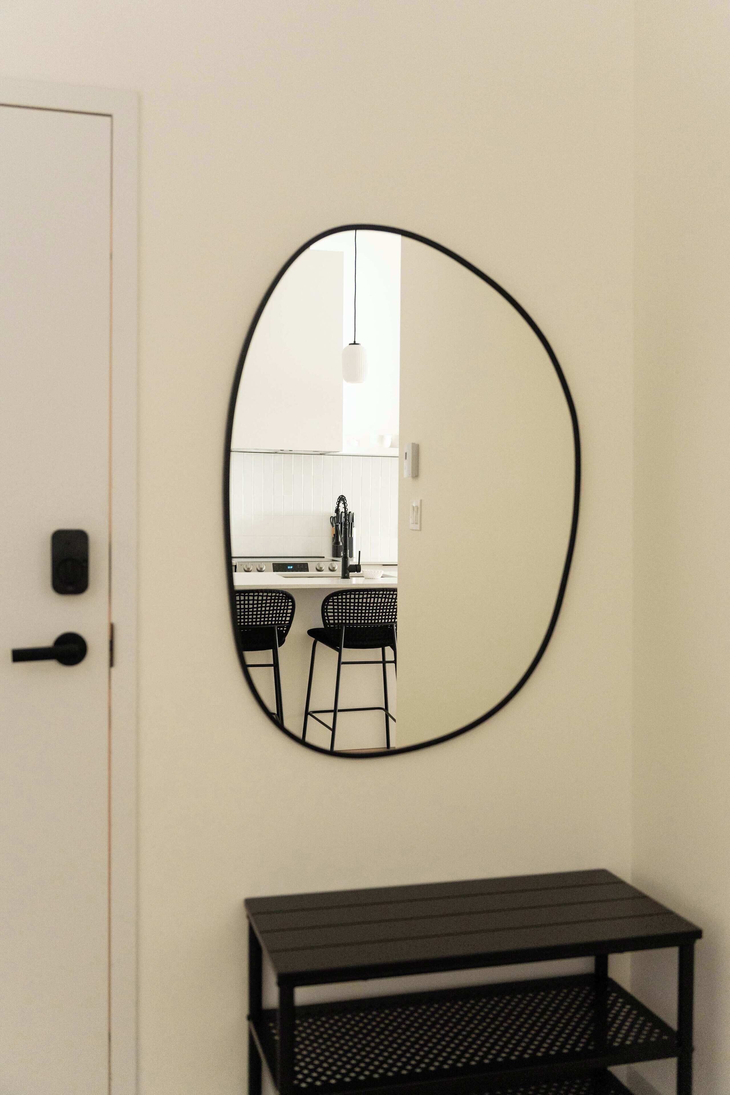 Quarto com porta branca, espelho com moldura preta na parede e mesa de metal preta com prateleiras.