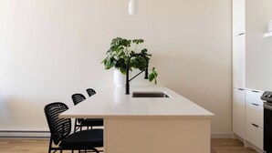 A modern kitchen with a white countertop, black chairs, a potted plant, and a hanging light fixture.