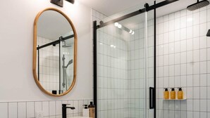 Un bagno moderno con un mobile lavabo bianco, cabina doccia in vetro e uno specchio con cornice in legno.