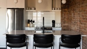 Una cucina moderna con isola centrale, sedie nere, frigorifero in acciaio inossidabile e parete in mattoni.