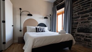 Un letto rifatto con lenzuola bianche e una testiera nera, una lampada da comodino e una pila di asciugamani piegati.