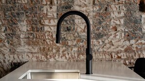 A modern kitchen with a sleek black faucet and a stainless steel sink against a textured stone wall.