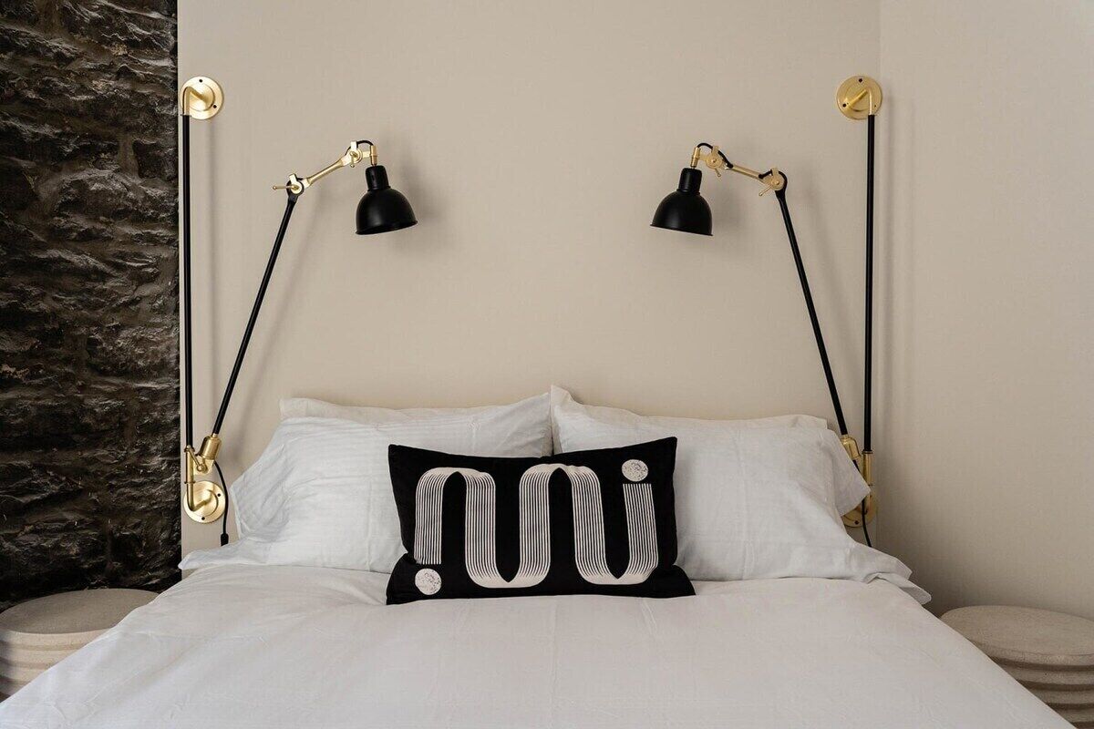 Ein Bett mit weißer Bettwäsche, ein schwarzes Kopfkissen mit weißem Muster und zwei schwarze Nachttische mit goldfarbenen Akzenten.