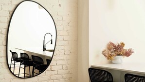 A room with a white brick wall, a round mirror, a dining table with black chairs, and a vase with dried flowers on a white shelf. - Maison Place Jacques-Cartier • Luxury One-Bedroom Apartment • Old Montreal • Freestanding bath • Full Kitchen • Skylight • Wi-Fi • AC (Montréal)
