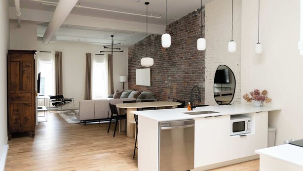 A modern kitchen with a white island, a brick accent wall, and pendant lighting. - Maison Place Jacques-Cartier • Luxury One-Bedroom Apartment • Old Montreal • Freestanding bath • Full Kitchen • Skylight • Wi-Fi • AC (Montréal)