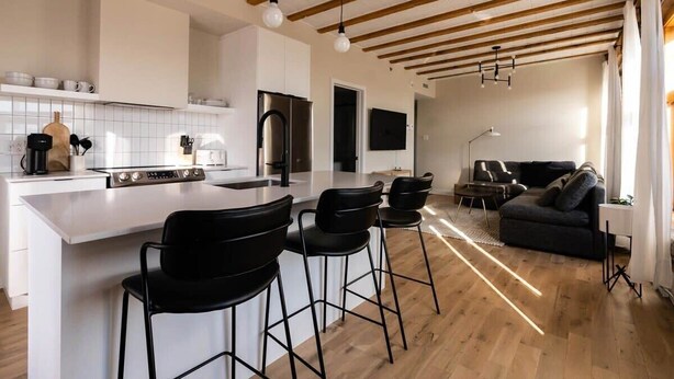 A modern kitchen with a central island, bar stools, and a dining area with a sofa. - Maison Place Royale • Luxury Waterfront Two-Bedrooms Apartment • Old Montreal • Water View St. Lawrence River • Full Kitchen • Stone Walls • Wi-Fi • AC (Montréal)