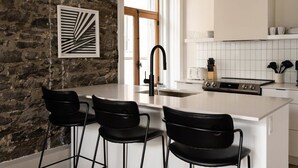 Une cuisine moderne avec un mur en pierre, une grande fenêtre et un coin bar agrémenté de trois chaises noires.