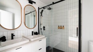Une salle de bain moderne avec deux lavabos, un grand miroir et une douche à parois de verre.