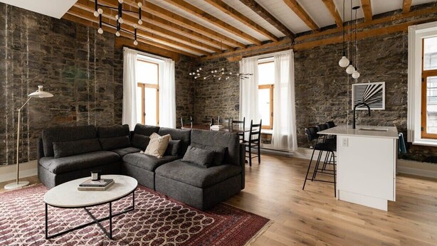 Un salon moderne avec un canapé d’angle, une table basse ronde et un îlot de cuisine.