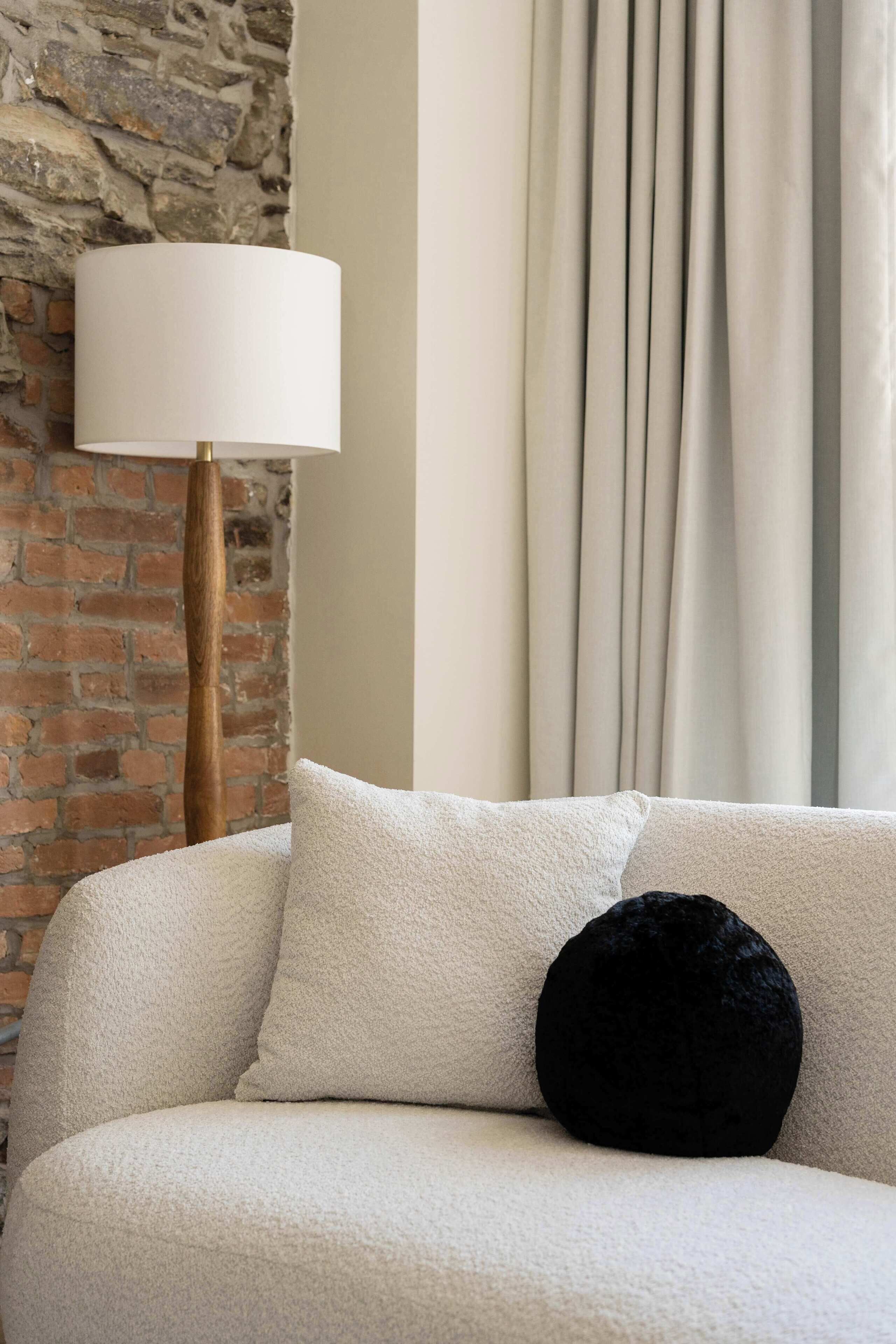 Un salon chaleureux avec un mur en briques, un canapé blanc agrémenté d’un coussin noir et un lampadaire.