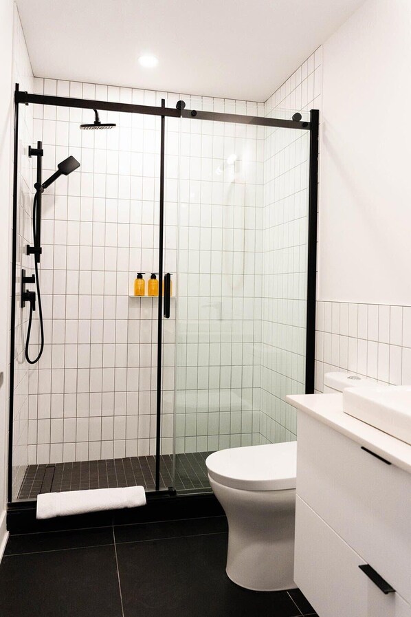 A modern bathroom with a glass-enclosed shower, a toilet, and a white sink.