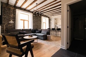 Una sala moderna con pared de piedra, vigas de madera, un sofá seccional, una mesa de centro redonda y un área de comedor con taburetes de bar.