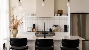 Una cocina moderna con una isla central, sillas negras, estufa y lámparas colgantes.