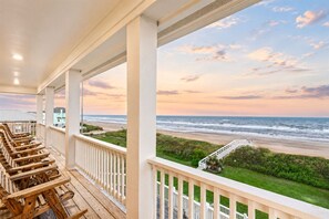 A covered outdoor area with wooden benches, a white railing, and a view of the beach and ocean.