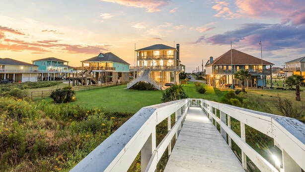 A coastal property with a wooden boardwalk leading to a large house with multiple levels and a balcony. - Beachfront | Hot Tub | Tiki Bar | Fenced Yard (Crystal Beach)