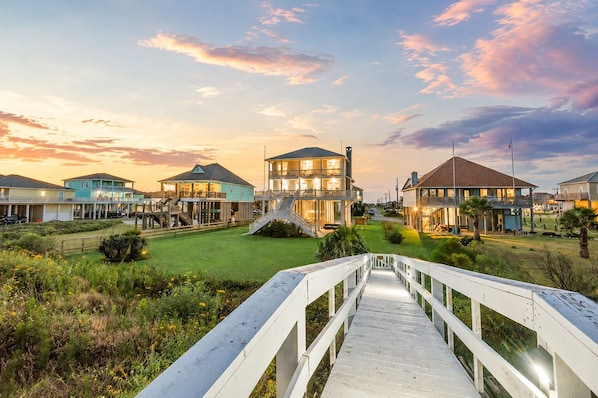 A coastal property with a wooden boardwalk leading to a large house with multiple levels and a balcony.