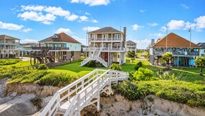 A beachfront hotel with multiple-story buildings, a central staircase, and a well-maintained lawn. - Beachfront | Hot Tub | Tiki Bar | Fenced Yard (Crystal Beach)