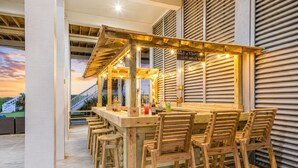 An outdoor bar area with wooden furniture and a view of a house in the background. - Beachfront | Hot Tub | Tiki Bar | Fenced Yard (Crystal Beach)