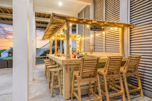 An outdoor bar area with wooden furniture and a view of a house in the background.