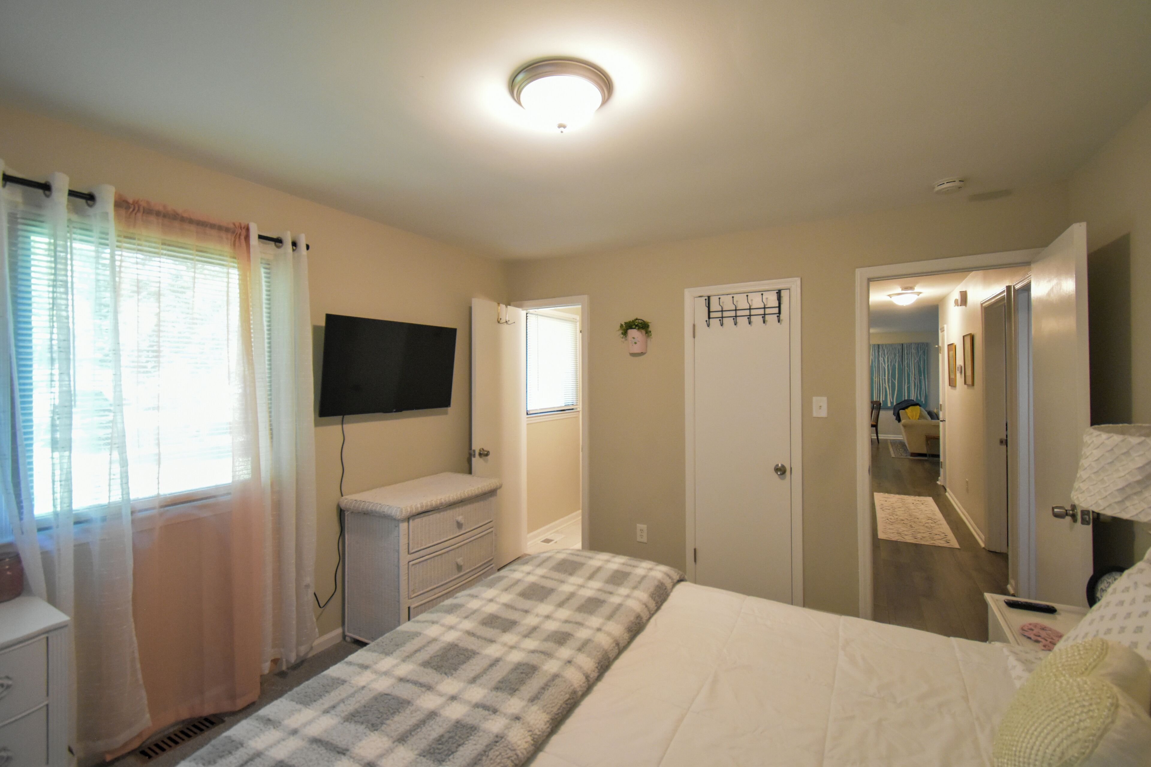 A bedroom with a bed, a dresser, a television, and a door leading to another room.