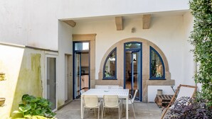 Un edificio de dos pisos con un patio que incluye una mesa, sillas, un pequeño jardín y vista a la calle.